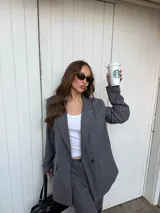 Conjunto de blazer y pantalón de lino gris con diseño de rayas diplomáticas. El blazer es de corte amplio con doble botonadura, y el pantalón es de corte recto y tiro alto.