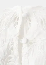 Blusa de encaje blanco con diseño floral, cuello alto y mangas largas con hombreras. Presenta un corte ajustado y acabado delicado.