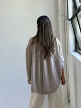 Poncho de tejido de punto color visón, con cuello alto y diseño de trenzas verticales. Presenta mangas cortas ajustadas y un corte holgado y redondeado en el ruedo.