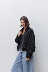 Campera marrón de poliuretano con acabado texturizado, silueta relajada, cuello camisero, cierre frontal, hombros caídos y mangas amplias con efecto abombado.