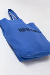 Tote bag de tela azul con estampado de la inscripción 'New York' en negro, diseño amplio con doble asa de hombro.