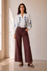 Camisa blanca de manga larga con bordados florales en tono rojo y verde en el frente y las mangas. Presenta cuello mao con escote en V y botones frontales.