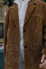 Chaqueta larga de piel color marrón, con cuello solapa, manga larga, bolsillos delanteros de plastrón y cierre frontal con botones.