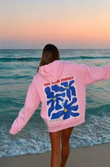 Canguro oversize color rosado, con capucha, mangas largas y bolsillo tipo canguro. Presenta un gran estampado en la espalda con flores azules y la leyenda "USE YOUR ENERGY".