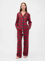 Conjunto de pijama compuesto por una camisa de manga larga con cuello solapa, cierre frontal de botones y bolsillo en el pecho, y un pantalón de corte recto con cintura elástica. Ambas piezas presentan un estampado de pequeños motivos oscuros sobre fondo claro y detalles de ribetes en contraste.