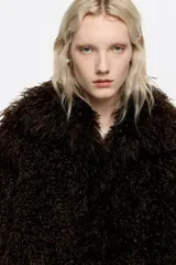 Abrigo de corte oversize confeccionado en pelo sintético de textura suave y voluminosa. Presenta cierre frontal con botones de presión, maxicuello camisero y mangas largas rectas. Incluye bolsillos laterales integrados en la costura.