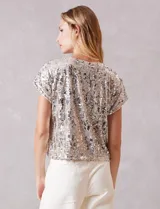 Blusa de manga corta cubierta de lentejuelas en tono champagne, con cuello redondo a la base y forro interno a tono.