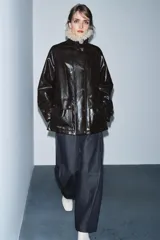 Chaqueta de efecto cuero color marrón oscuro con acabado brillante, cuello de solapa con aplicación de pelo sintético extraíble, manga larga con trabillas, bolsillos frontales de plastrón con solapa y cierre frontal con cremallera y botones a presión.