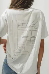 Remera blanca de algodón orgánico con estampa lineal en la espalda que representa una escena de interior con mobiliario y sombrillas.