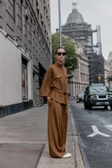 Camisa de estilo safari en color marrón con efecto ante, cuello subido y mangas anchas de largo tres cuartos con terminación en vuelta. Presenta bolsillos con solapa en el pecho, cintura ajustable con lazo del mismo tejido y cierre frontal oculto con cremallera y botones a presión.