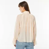 Camisa vaporosa color beige claro, con cuello alto y lazo al cuello, mangas largas abullonadas con puños elásticos.