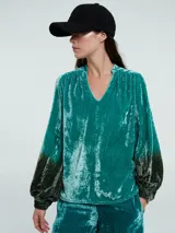 Blusa verde esmeralda de terciopelo con escote en V y mangas largas abullonadas con degradé a negro en los puños.