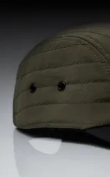 Gorra de estilo 5 paneles, color verde militar, con corona acolchada y visera negra. Presenta un pequeño parche negro con un logo blanco en forma de tijeras cruzadas.