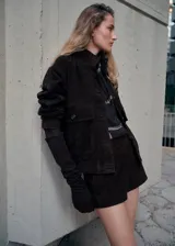 Chaqueta marrón oscuro de piel caprino, con cierre frontal de botones, bolsillos con solapa en el pecho y mangas largas.