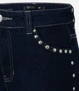 Pantalón loose de cintura baja confeccionado en jeans azul oscuro, con trabillas en la cintura, cierre tradicional, bolsillos y tachas aplicadas desde los bolsillos delanteros hasta los laterales.