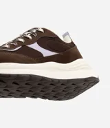 Championes estilo runner de la marca Satinato, confeccionadas en una combinación de poliuretano y mesh respirable. Presentan un diseño con recortes superpuestos en tonos marrón y detalles en lila, cierre con cordones bicolor, lengüeta acolchada, tirador trasero y una suela robusta con entresuela alta y base tractorada.