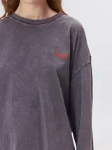 Remera oversize de manga larga color naranja con efecto gastado, cuello redondo y gráfico estampado en la espalda.