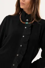 Camisa negra de textura sutil, con cuello alto tipo mao, cierre frontal con botones y detalle de volado lateral. Presenta mangas largas con puños con volados.