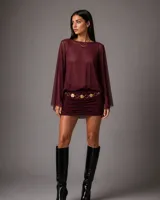 Vestido corto color bordó, con cuerpo superior de gasa transparente de manga larga y falda ajustada con frunces laterales. Incluye un cinturón decorativo de eslabones metálicos dorados.