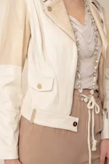 Chaqueta corta cruzada de cuero vegano color marfil, combinada con tela rayada color oro, con cierres metálicos y tachas doradas.