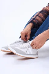 Championes urbanos de diseño retro, combinan paneles de cuero sintético y gamuza en tonos blanco y gris claro. Presentan cordones al tono, suela de goma dentada en color caramelo y detalles laterales de franjas.