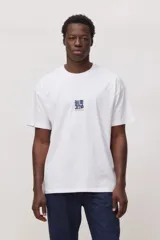 Remera de manga corta color blanco, con cuello redondo y diseño holgado. Presenta un pequeño estampado gráfico centrado en el pecho con el logo de la marca.