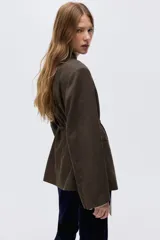 Blazer cruzado con estampado de pata de gallo en tonos marrón y negro. Presenta cuello elevado, hombreras, abertura en los puños, bolsillos delanteros ribeteados y un cinturón fino para ajustar la cintura. Está forrado.