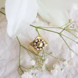 Anillo de bronce con forma cuadrada y diseño de margarita con centro dorado y pétalos plateados.