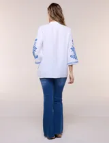 Blusa blanca con bordados florales en azul, de manga tres cuartos y cuello mao con escote en V.