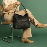 Cartera tipo hobo de cuero sintético color rojo ladrillo, con correa de hombro ajustable. Tiene cierre superior con solapa y broche magnético, bolsillo frontal con cierre, bolsillos laterales con cierre y múltiples bolsillos internos.