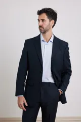 Traje de corte clásico compuesto por saco de dos botones y pantalón de vestir a juego. El saco presenta solapas tradicionales y bolsillos con solapa, mientras que el pantalón tiene un corte recto y formal.