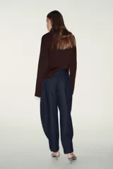 Pantalón de denim azul oscuro, tiro alto, con pinzas delanteras que generan volumen en la cadera y pernera ancha y recta. Presenta cierre frontal y bolsillos laterales.