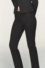 Pantalón entallado de tiro alto color negro, con cintura con trabillas y bolsillos de vivo con cremallera en el delantero. El bajo tiene un acabado en línea evasé. Cierre frontal con cremallera, botón interior y gancho metálico.