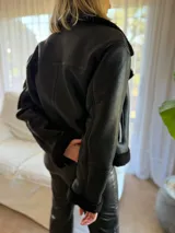 Campera de gamulán color marrón chocolate, con interior y detalles en corderito al tono. Presenta cierre frontal cruzado, cuello solapa amplio y bolsillos laterales con cierre metálico.