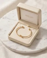 Pulsera tipo esclava rígida de acero con baño de oro, con un diseño minimalista que presenta un detalle de nudo central.