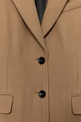 Abrigo largo entallado de Zara Woman Collection, confeccionado en mezcla de lana color tostado. Presenta cuello con solapa de muesca, mangas largas, bolsillos con solapa en el frente, forro interior y cierre frontal de dos botones oscuros.