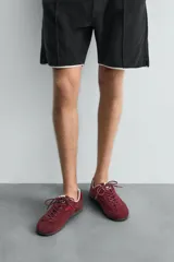 Zapatilla de cordones de estilo retro, con parte superior de serraje color bordó y detalles en piel lisa color rojo. Suela ultrafina de goma en tono marrón oscuro.