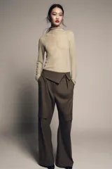 Pantalón de tiro medio color marrón oscuro, estilo cargo, con cintura acabada en vuelta asimétrica, pliegues delanteros y bolsillos laterales y con solapa en las piernas.