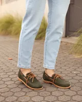 Zapatos náuticos de cuero verde oscuro, estilo mocasín con cordones de cuero marrón claro, costuras visibles en contraste y suela plana.