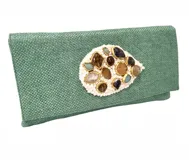 Bolso tipo sobre en yute de algodón color verde turquesa con cierre frontal y aplique bordado en piedras de diferentes colores. Posee asa de cadena larga desmontable para llevar tipo bandolera o al hombro.