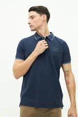 Polo de manga corta Brooksfield en color azul marino con textura. Presenta cuello clásico con cierre de botones, logo estampado en el pecho y detalles en contraste en el borde del cuello y las mangas.