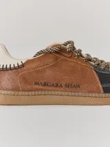 Championes de cuero con diseño tricolor en tonos negro, marrón y crema. Presentan cordones trenzados, costuras a la vista y detalle de pespuntes en el talón.