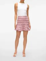 Pollera corta de tiro alto confeccionada en tejido de tweed con diseño a cuadros. Presenta un corte ajustado en la parte superior con un detalle de volado en el ruedo.