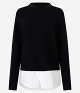 Suéter negro de punto con cuello redondo y mangas largas. Tiene un dobladillo superpuesto de camisa blanca.