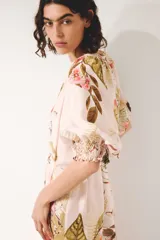 Vestido midi oversized de mezcla de viscosa, con estampado floreado tropical sobre base rosada, escote en V y botonadura frontal. Cuenta con mangas al codo raglán con puños fruncidos, cinturón fino para atar con cuentas y diseño escalonado en la falda.