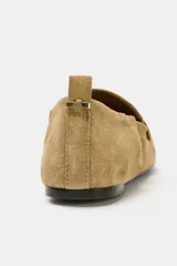 Mocasín de serraje color tostado, con copete subido, antifaz en la parte delantera y detalle fruncido en la parte trasera con tirador y aplique metálico.