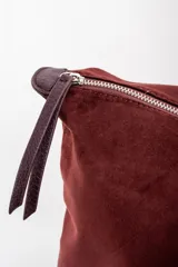 Bolso tipo tote de gran tamaño en color bordó, confeccionado en material sintético con textura de gamuza. Cuenta con cierre superior, correas largas de hombro en tono marrón oscuro y una placa metálica decorativa en el frente.