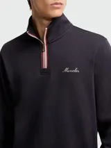 Buzo de algodón color negro con capucha integrada, cierre frontal parcial con cremallera y detalle de cinta tricolor. Presenta una capa interior en color verde con puños y ruedo elásticos, y el logo de la marca bordado en el pecho.