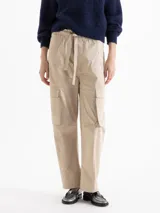 Pantalón cargo de corte recto y largo al tobillo, color beige. Presenta cintura elastizada con lazo ajustable, bolsillos laterales con tapa estilo utilitario y bolsillos adicionales en el delantero y la espalda.