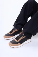 Championes urbanos de diseño moderno, combinando paneles en color negro y tostado. Presentan cordones negros, suela blanca con base en color tostado y una estructura versátil para uso diario.